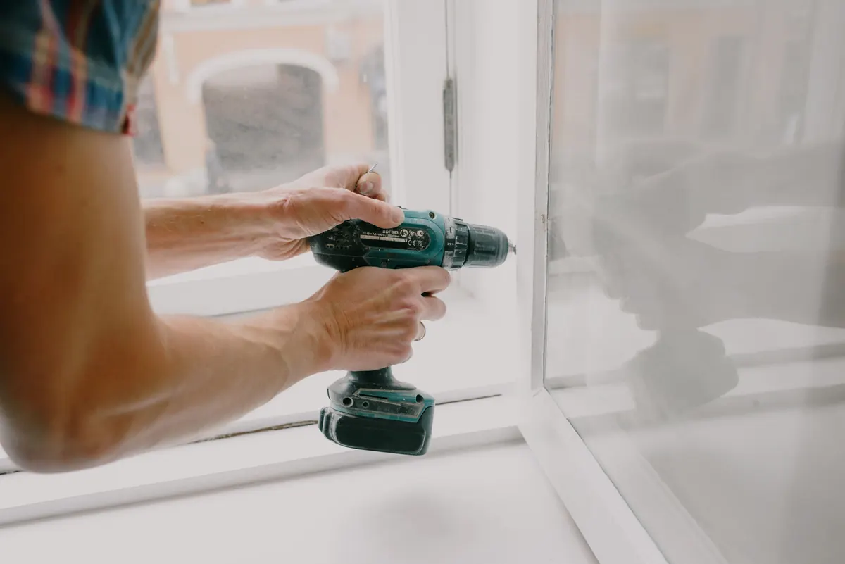 Tradesperson using a power drill to carry out property maintenance work on a window